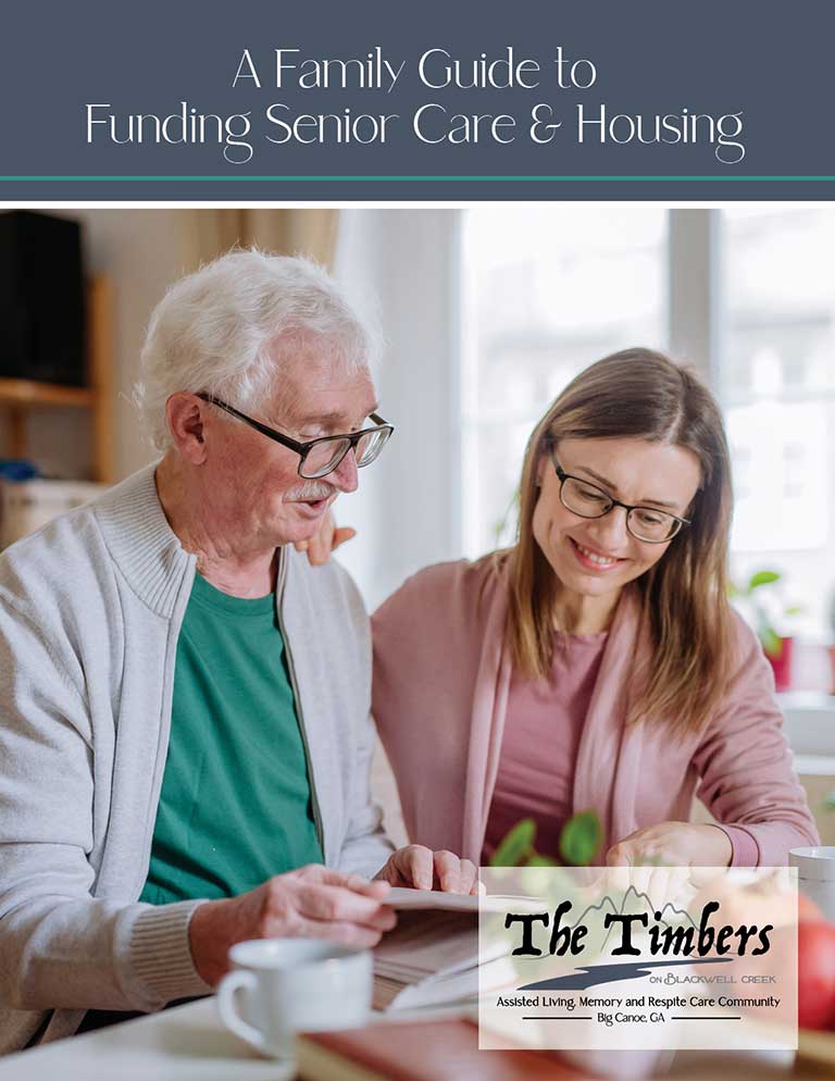 Older man and younger woman looking at documents together at a table, with a brochure titled "A Family Guide to Funding Senior Care & Housing" from The Timbers.