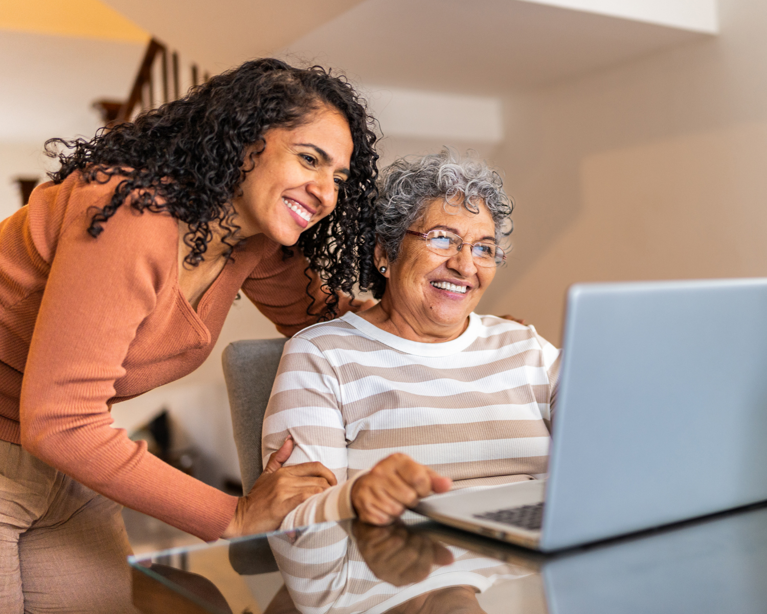 An elderly woman and her adult daughter look at a laptop.
